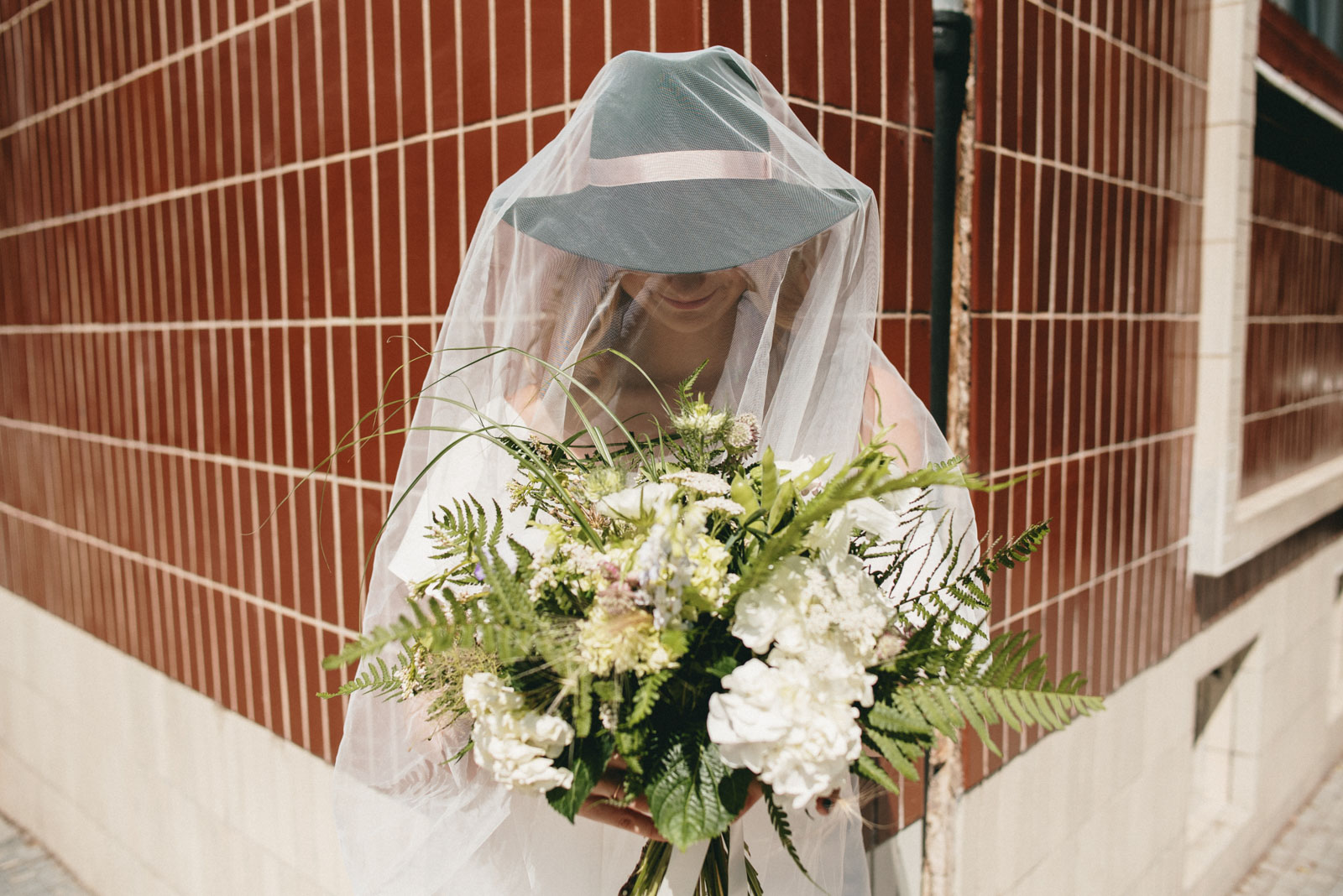 nevěsta zahalená do závoje drží svatební kytici z lučního kvítí a kapradin